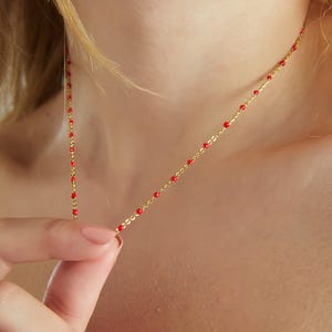 May include: A gold chain necklace with small red beads. The necklace is delicate and simple.