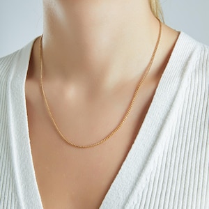 May include: A gold chain necklace on a person wearing a white sweater.