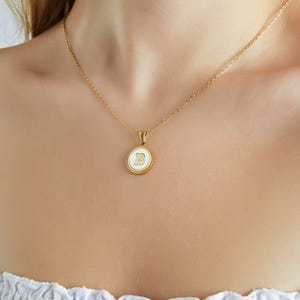May include: A gold chain necklace with a white pendant featuring the letter "B" in gold.