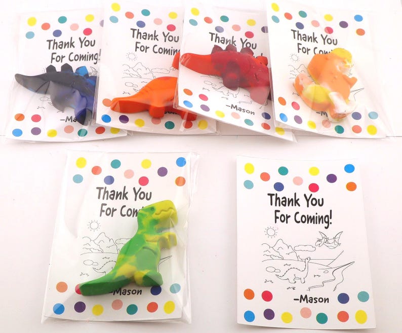 May include: A collection of dinosaur-shaped crayons in clear plastic bags, each paired with a card that reads "Thank You For Coming!" in black text. The crayons are various colors, including blue, orange, and green.