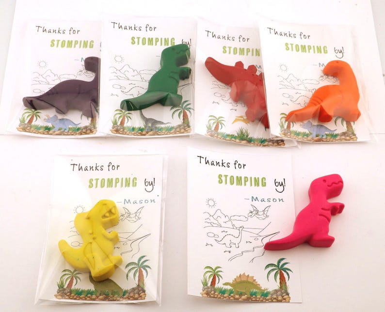 May include: Six colorful dinosaur-shaped crayons in clear cellophane bags. Each bag has a card with the text "Thanks for STOMPING by!" and a dinosaur illustration. Colors include purple, green, red, orange, yellow, and pink.