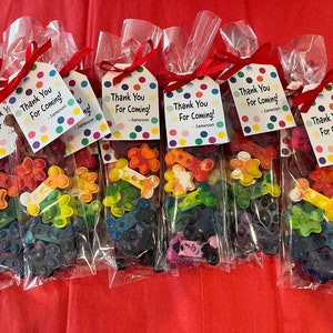 May include: Seven clear plastic bags filled with colorful crayon shaped like bones. Each bag has a white tag with colorful polka dots and the text "Thank You For Coming! - Jameson".