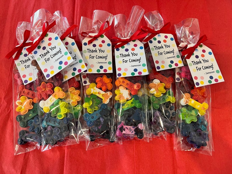 May include: Seven clear plastic bags filled with colorful crayon shaped like bones. Each bag has a white tag with colorful polka dots and the text "Thank You For Coming! - Jameson".