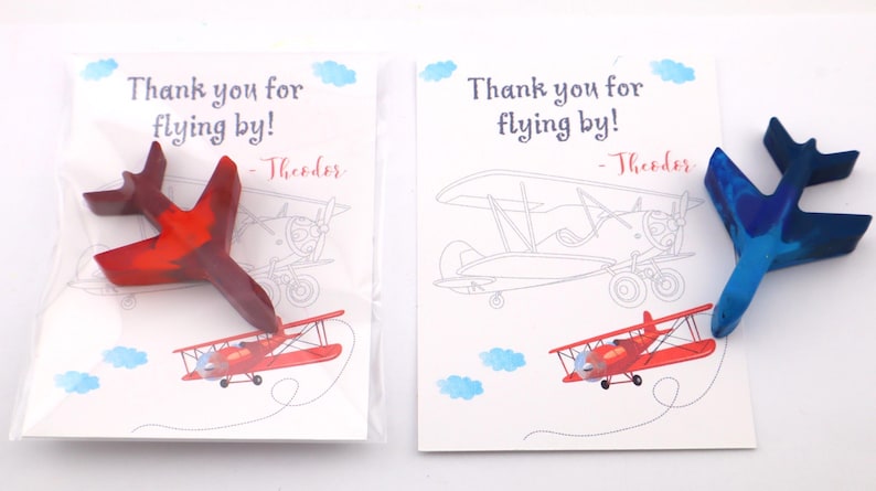 Puede incluir: Dos crayones con forma de avi&oacute;n, uno rojo y otro azul, descansan sobre tarjetas con ilustraciones de aviones y el texto "Thank you for flying by!" y un nombre. Las tarjetas tienen acentos de nubes azules.