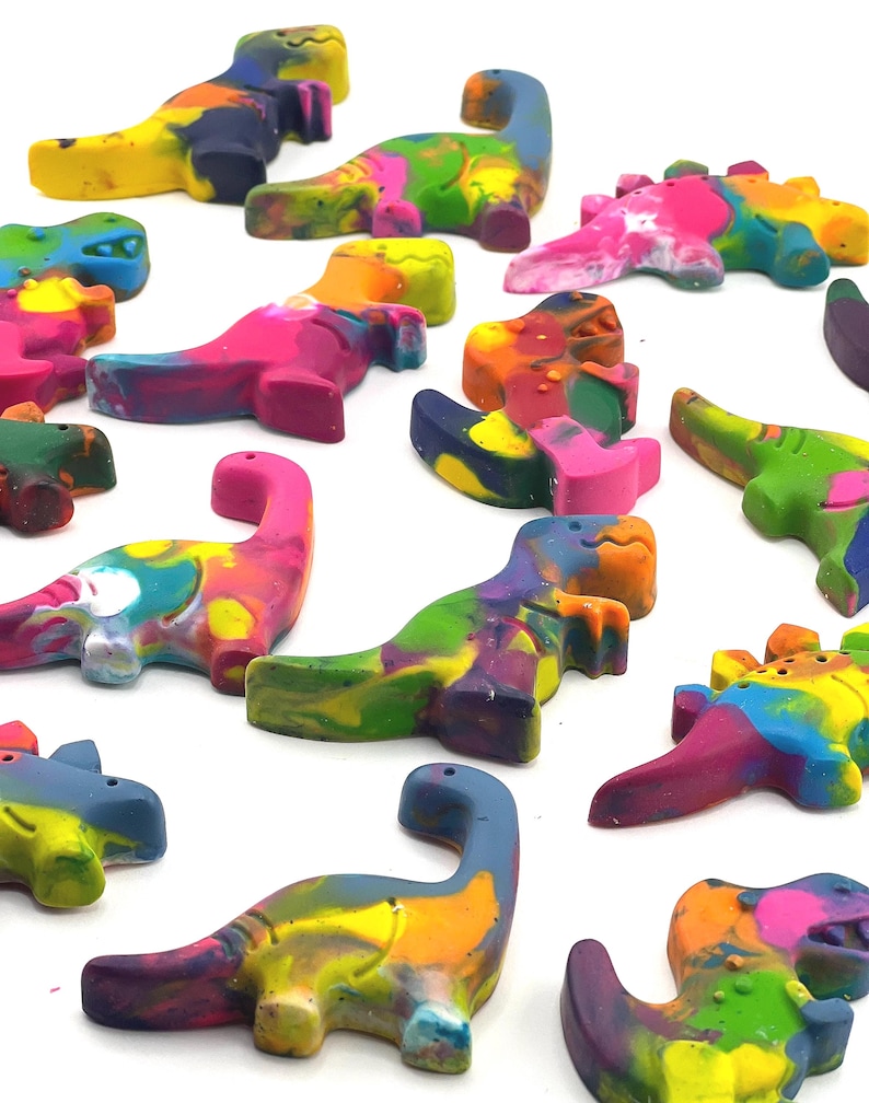 May include: A collection of colorful dinosaur-shaped crayons in various shades of pink, blue, yellow, green, and orange. The crayons are arranged on a white surface, showcasing their vibrant, multi-colored appearance. These crayons are ideal for children's art projects.
