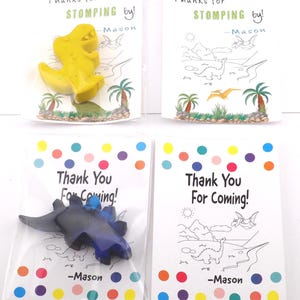 May include: Four small party favor bags. Two bags have yellow dinosaur crayons with the text "Thanks for STOMPING by!" and "-Mason". The other two bags have blue dinosaur crayons with the text "Thank You For Coming!" and "-Mason".
