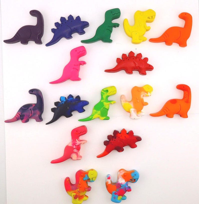 May include: A collection of colorful dinosaur-shaped crayons in various shades, including purple, blue, green, yellow, orange, and pink. The crayons are arranged on a white surface, showcasing their different shapes and sizes. These crayons are perfect for creative projects.