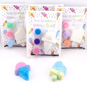 May include: Three clear plastic bags with ice cream-themed craft kits. Each kit includes a white ice cream-shaped item, paint pots, and the text "Thanks for making my Birthday so Sweet! - Emi & Lily." Two colorful ice cream treats are in front.