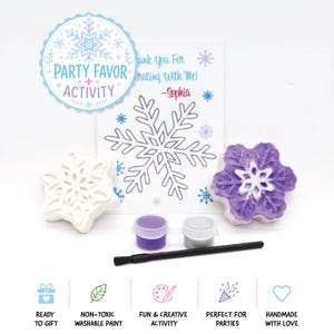 May include: A snowflake-themed craft kit featuring a white snowflake-shaped plaster figure, a purple and white snowflake-shaped plaster figure, two small paint pots in purple and silver, a black paintbrush, and a card with a snowflake outline.