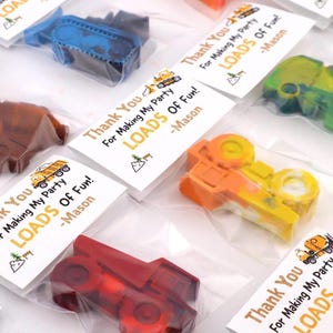 May include: Multiple construction vehicle-shaped crayons in clear plastic bags, each with a white tag reading Thank You For Making My Party LOADS OF FUN! -Mason. The crayons are in various colors including blue, brown, green, orange, and red.