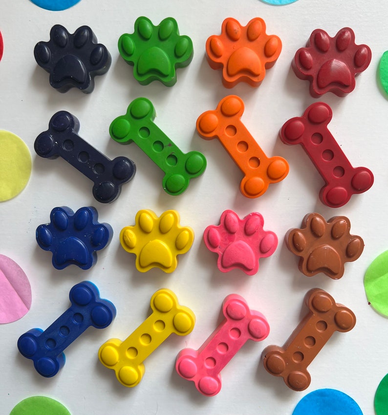 May include: Assortment of colorful crayons shaped like dog paws and bones. The crayons are arranged in two rows on a white surface.