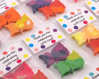 May include: Colorful butterfly-shaped crayons packaged in clear plastic bags with thank you tags. The tags have a polka dot pattern and the text "Thank you for celebrating with Lena!"
