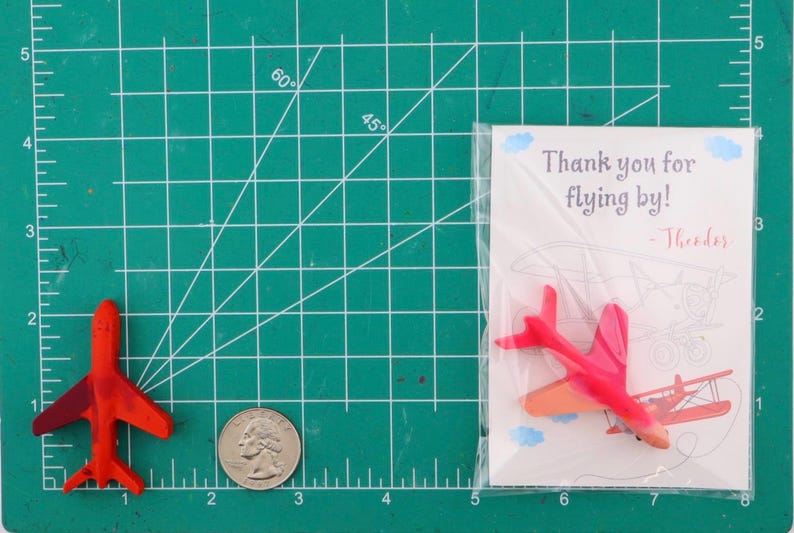 Puede incluir: Una esterilla de corte verde muestra un avi&oacute;n de juguete rojo, una moneda y una tarjeta. La tarjeta dice "Thank you for flying by!" con una ilustraci&oacute;n de avi&oacute;n. El avi&oacute;n es rojo con alas rojo oscuro. Medidas en cent&iacute;metros.