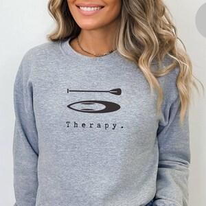 以下が含まれることがあります： パドルボードのグラフィックと「Therapy.」というテキストがプリントされたグレーのスウェットシャツ。ウエストバンドは腰にフィットし、たるみません。スウェットシャツはオーバーサイズで、1サイズまたは2サイズ大きくても着用できます。