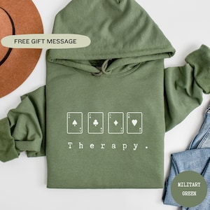 May include: A green hooded sweatshirt with the text "Therapy." and four playing card symbols: a spade, a club, a diamond, and a heart.