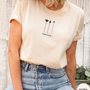 This natural t-shirt has a black image of three paintbrushes centred in the middle, with the word therapy underneath. Tailored towards people who enjoy painting also who find painting a form of therapy.