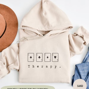 This sand hoodie has a black image of playing cards centred in the middle, with the word therapy underneath. Tailored towards people and couples who enjoy playing cards games also who find playing card games a form of therapy.