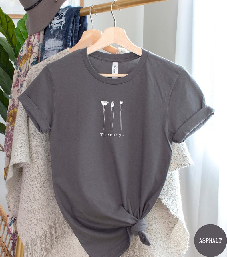 This asphalt t-shirt has a white image of three paintbrushes centred in the middle, with the word therapy underneath. Tailored towards people who enjoy painting also who find painting a form of therapy.