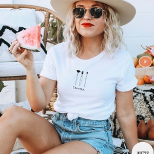 This white t-shirt has a black image of three paintbrushes centred in the middle, with the word therapy underneath. Tailored towards people who enjoy painting also who find painting a form of therapy.