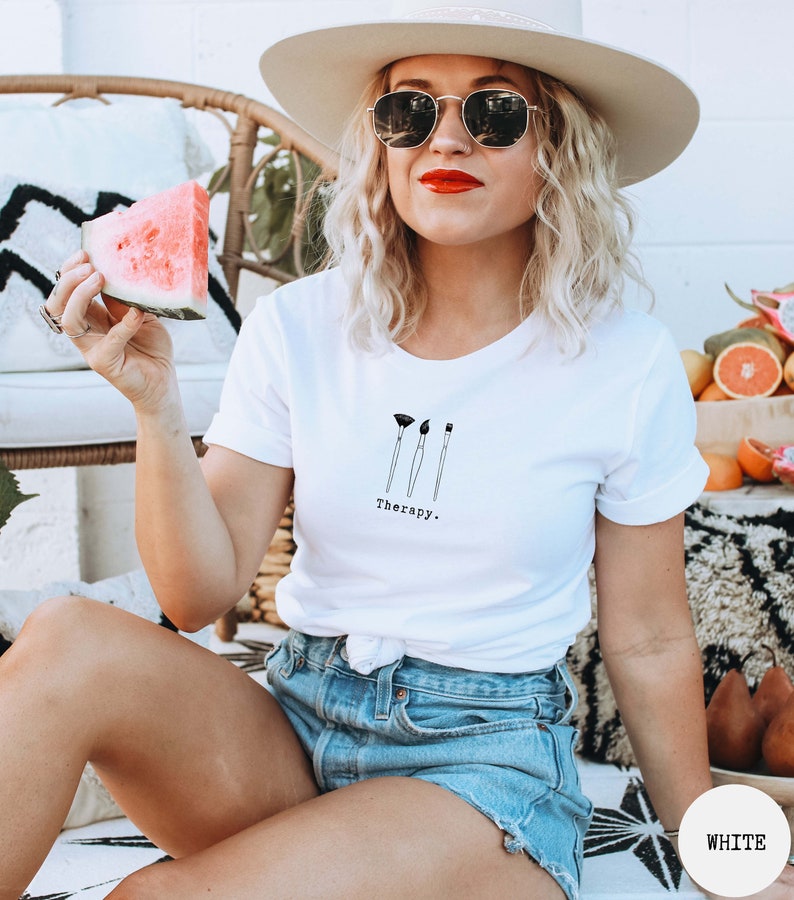 This white t-shirt has a black image of three paintbrushes centred in the middle, with the word therapy underneath. Tailored towards people who enjoy painting also who find painting a form of therapy.