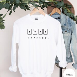 This white sweatshirt has a black image of a playing cards centred in the middle, with the word therapy underneath. Tailored towards people who enjoy playing cards also who find card games a form of therapy