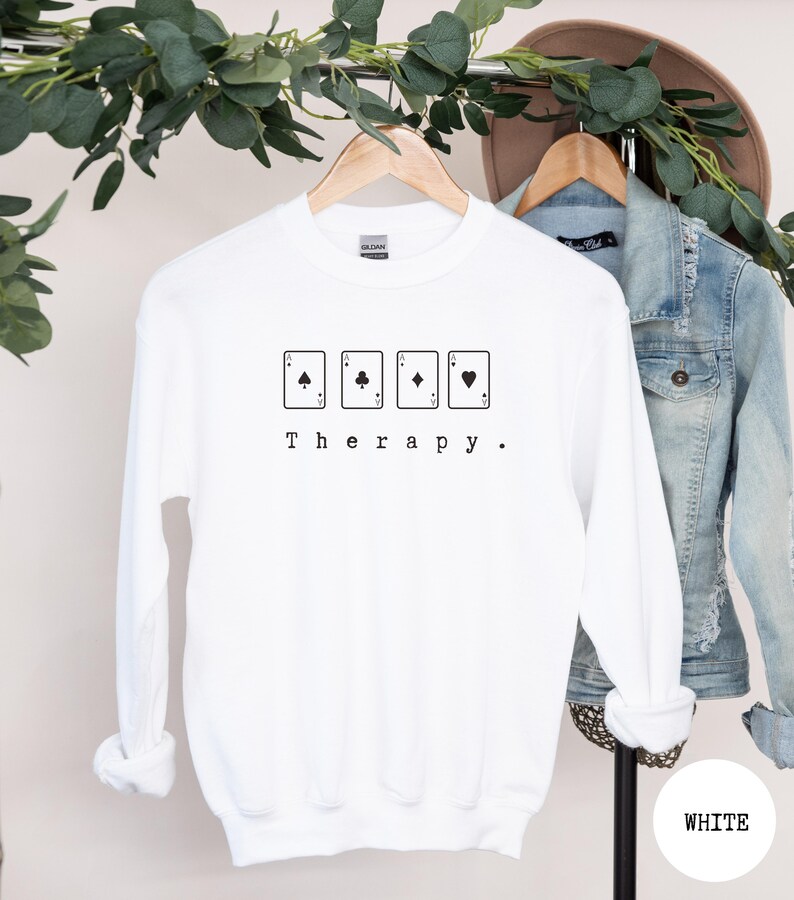 This white sweatshirt has a black image of a playing cards centred in the middle, with the word therapy underneath. Tailored towards people who enjoy playing cards also who find card games a form of therapy
