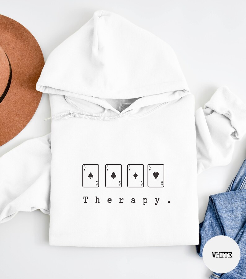 This white hoodie has a black image of playing cards centred in the middle, with the word therapy underneath. Tailored towards people and couples who enjoy playing cards games also who find playing card games a form of therapy.