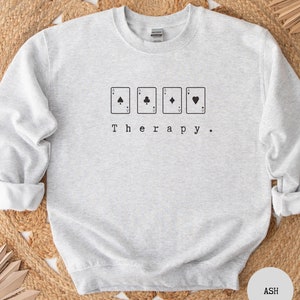 This ash sweatshirt has a black image of a playing cards centred in the middle, with the word therapy underneath. Tailored towards people who enjoy playing cards also who find card games a form of therapy