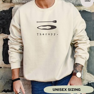 This sand sweatshirt has a black image of a sup board centred in the middle, with the word therapy underneath. Tailored towards people and couples who enjoy sup boarding also who find sup boarding a form of therapy.