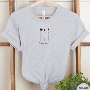 This athletic heather t-shirt has a black image of three paintbrushes centred in the middle, with the word therapy underneath. Tailored towards people who enjoy painting also who find painting a form of therapy.