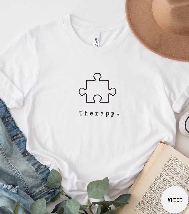 May include: White t-shirt with a black puzzle piece graphic and the text "Therapy."