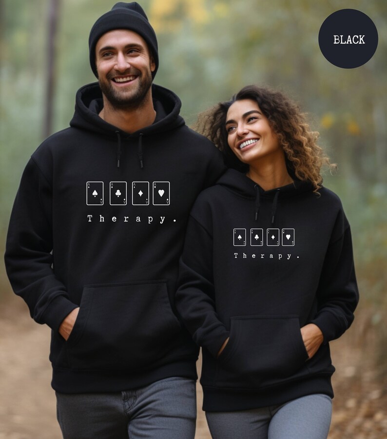 This black hoodie has a white image of playing cards centred in the middle, with the word therapy underneath. Tailored towards people and couples who enjoy playing cards games also who find playing card games a form of therapy.