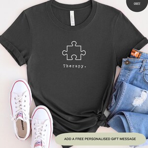 This dark grey t-shirt has a white image of a puzzle piece centred in the middle, with the word therapy underneath. Tailored towards people who enjoy puzzles also who find puzzles a form of therapy.