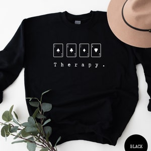 This black sweatshirt has a white image of a playing cards centred in the middle, with the word therapy underneath. Tailored towards people who enjoy playing cards also who find card games a form of therapy