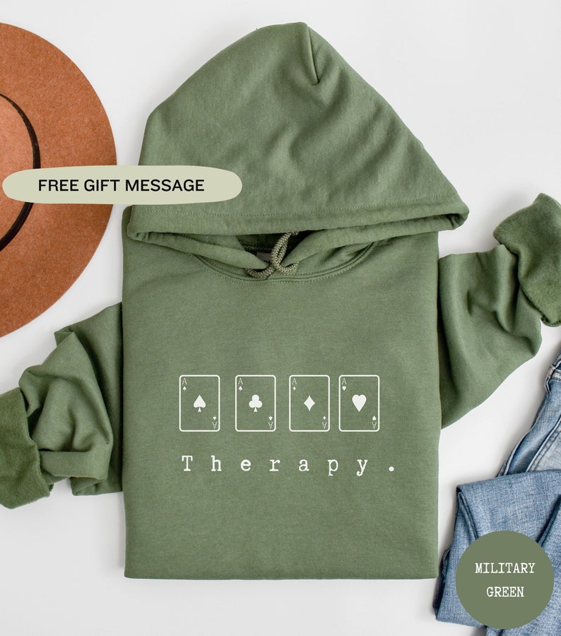 May include: A green hooded sweatshirt with the text "Therapy." and four playing card symbols: a spade, a club, a diamond, and a heart.