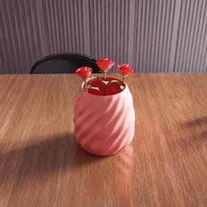 May include: A pink ceramic vase with a swirl design, holding three red paper roses.
