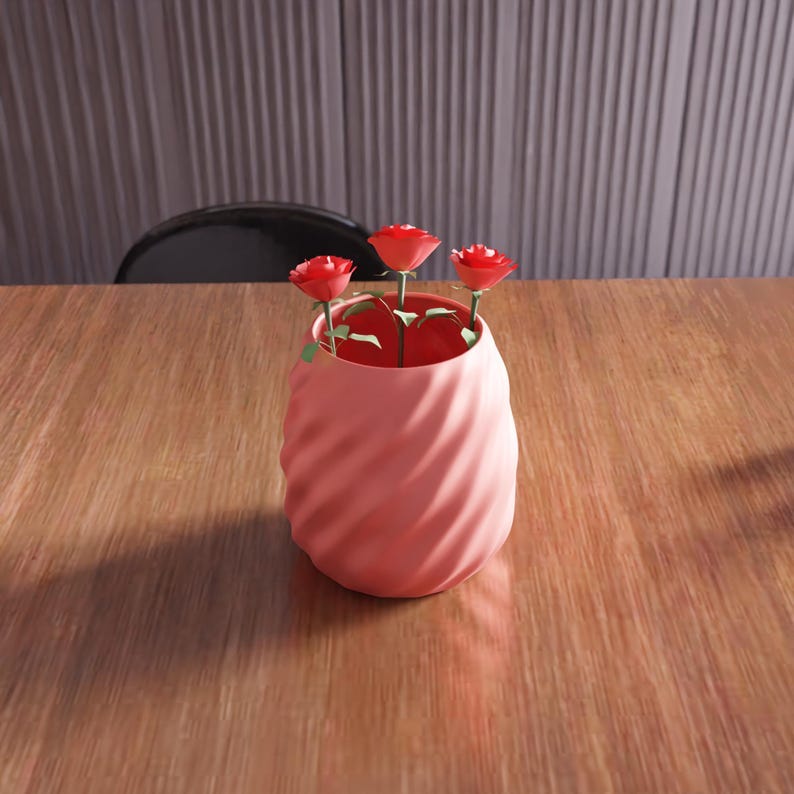 May include: A pink ceramic vase with a swirl design, holding three red paper roses.