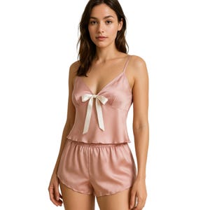 May include: A blush pink satin pajama set with a bow detail on the top. The set includes a cami top and shorts.