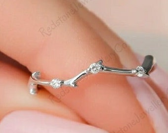 May include: A delicate silver ring with a branch-like design, adorned with small, sparkling gemstones. The ring's organic shape and minimalist style create an elegant and nature-inspired aesthetic. The ring is held by a person.