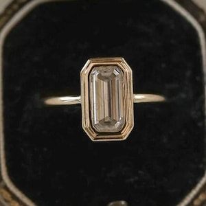 Anillo solitario de moissanita talla esmeralda, con engaste de bisel en oro amarillo de 14 quilates.