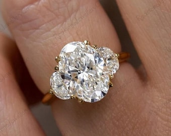 May include: A gold engagement ring with a large oval-shaped center diamond and two smaller round diamonds on either side. The ring is set in a delicate, ornate design.