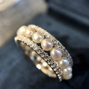 Puede incluir: Un anillo de plata con una doble fila de pequeñas perlas blancas y una fila de piedras de circonita cúbica transparentes.