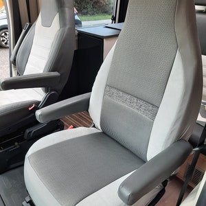 May include: Two-tone grey and white vehicle seats with armrests. The seats feature a textured fabric centre panel and smooth side panels. The armrests are a solid grey colour. The seats are in a vehicle interior.