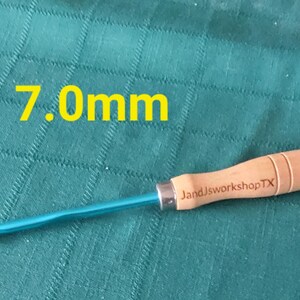 May include: A 7.0mm crochet hook with a blue metal hook and a wooden handle. The handle is engraved with "JandJworkshopTX".