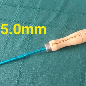 May include: A blue and wooden crochet hook with a 5.0mm size label and the text "JandJworkshopTX" on the wooden handle.