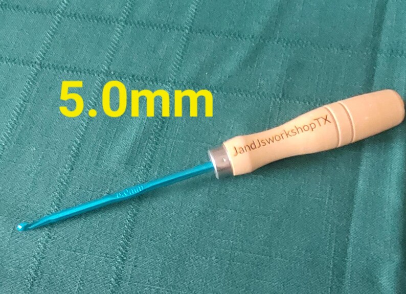 May include: A blue and wooden crochet hook with a 5.0mm size label and the text "JandJworkshopTX" on the wooden handle.