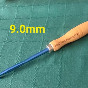 May include: A 9.0 mm crochet hook with a blue metal hook and a wooden handle. The handle is engraved with "JandJworkshopTX".