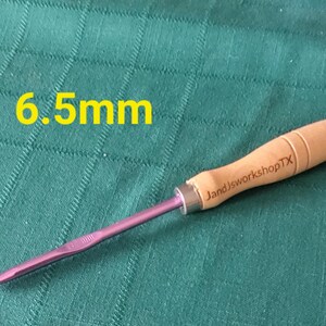 May include: A 6.5 mm crochet hook with a purple metal hook and a wooden handle. The handle is engraved with "JandJworkshopTX".