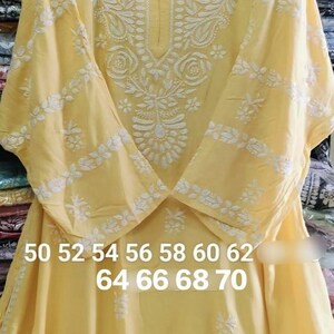 May include: A yellow embroidered tunic with white floral designs. The tunic has a V-neck and is hanging on a hanger. The size chart is visible at the bottom of the image: 50 52 54 56 58 60 62 64 66 68 70.