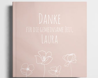 May include: A pink book with the text "DANKE FÜR DIE GEMEINSAME ZEIT, LAURA" in white. The book is decorated with white line drawings of flowers.